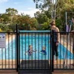 Family watching kids swim behind a compliant pool safety fence with CPR sign, Australian backyard summer